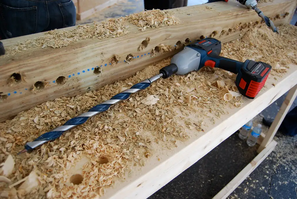 Close-up of a random orbital sander smoothing a hardwood edge beside a dust hose