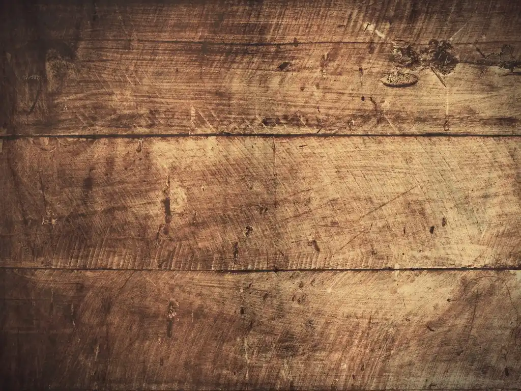 Homeowner comparing floor refinisher bottles beside a scratched hardwood sample in a sunlit room