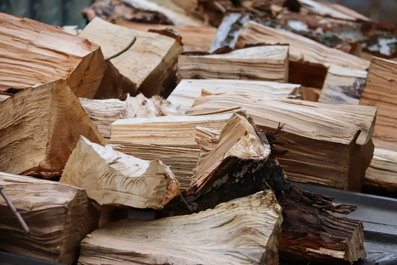 Split firewood stacked outdoors in a snowy winter yard beside a tarp-covered pile.