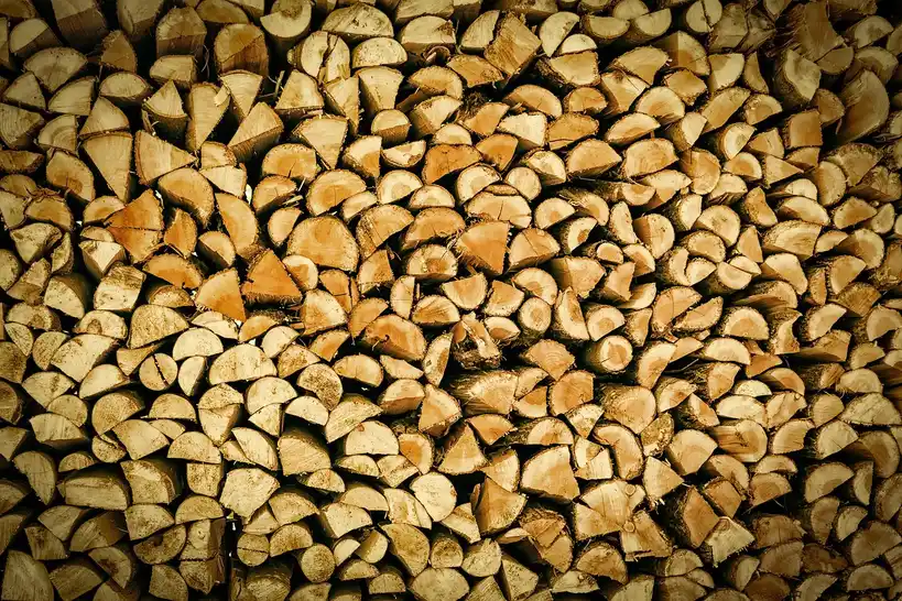 Very dry firewood stacked beside a wood stove with cracked ends and loose bark
