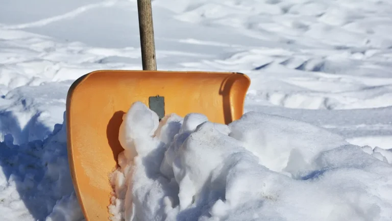 Homeowner brushing fresh snow off a wooden deck in winter light
