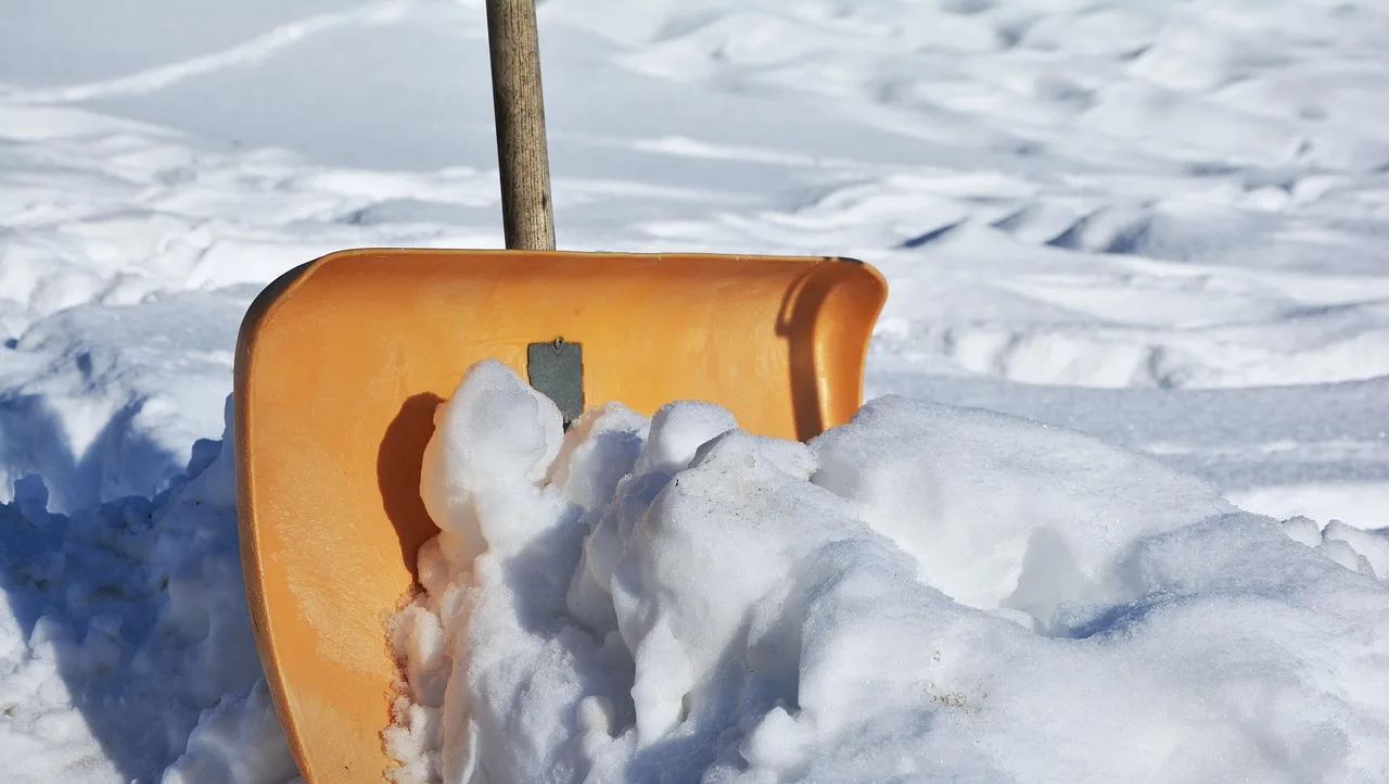 Homeowner brushing fresh snow off a wooden deck in winter light