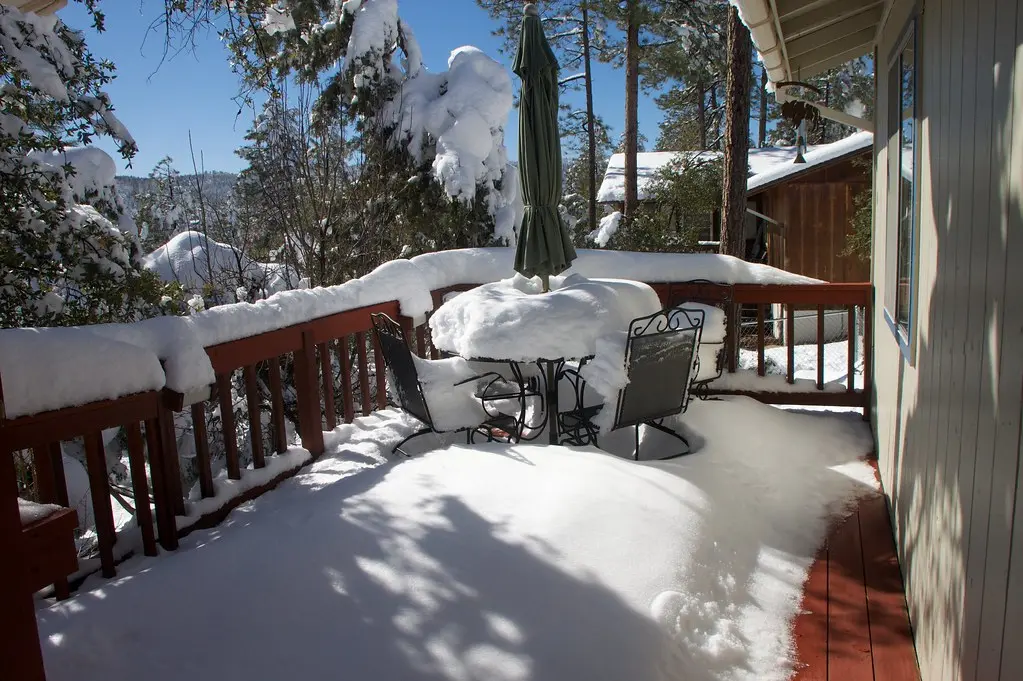 Close-up of a plastic shovel lifting snow from composite deck boards