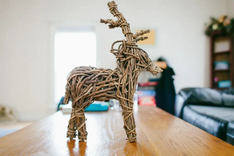Small wooden reindeer standing on a workbench in a sunlit workshop with tools and wood scraps nearby