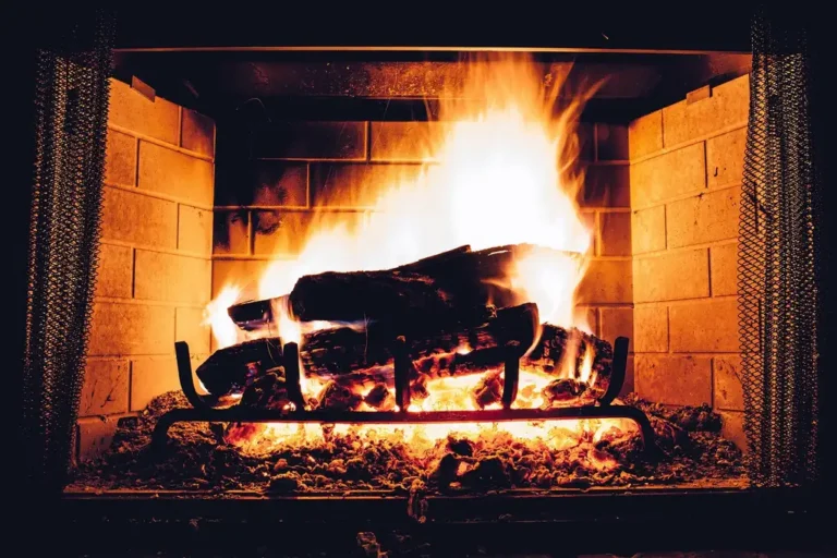Split poplar firewood stacked beside a small outdoor fire starting to burn