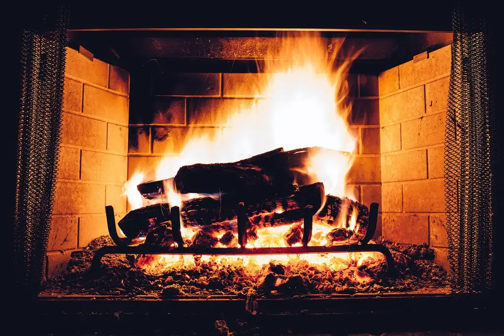 Split poplar firewood stacked beside a small outdoor fire starting to burn