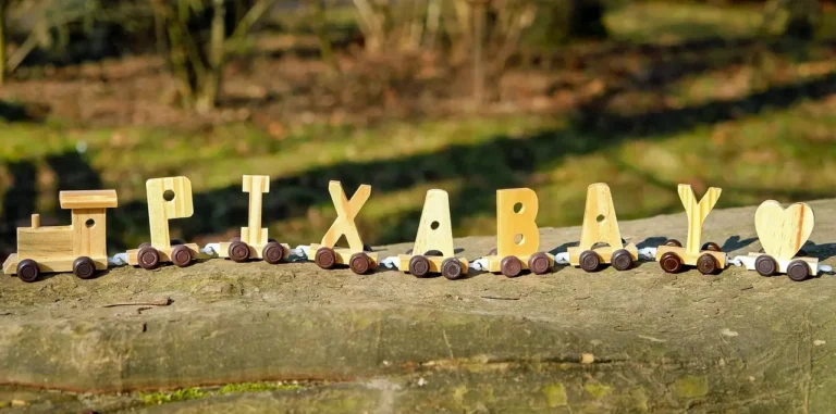 Painted wooden name ornaments, paint brushes, and blank wood pieces arranged on a craft table